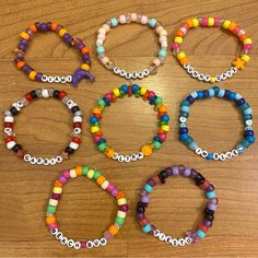 six bracelets with different colored beads are arranged on a wooden surface and have the word boo spelled in small letters