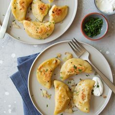 two white plates topped with dumplings next to a bowl of sour cream and a fork