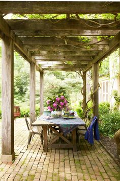 a table and chairs under a pergolated area with flowers on the table in vases