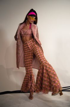 a woman in a pink and brown outfit is standing on a white surface with her hands behind her head