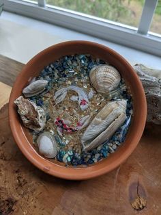 a bowl filled with sea shells on top of a wooden table next to a window