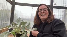 a woman in glasses is smiling next to a potted plant