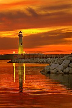 a light house sitting on top of a body of water next to a pier at sunset