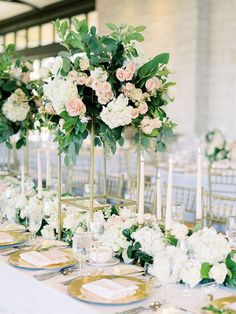 the table is set with white flowers and gold place settings for an elegant wedding reception