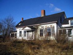 an old run down house sitting in the middle of a field with weeds growing around it