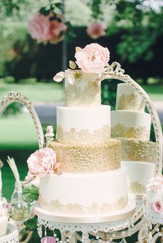 a white and gold wedding cake sitting on top of a table next to pink flowers