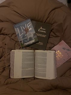 three books are laying on top of a brown comforter, one is open and the other is closed