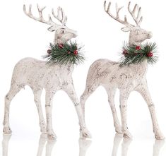 two white reindeer statues with red berries and pine cones on their antlers, standing next to each other