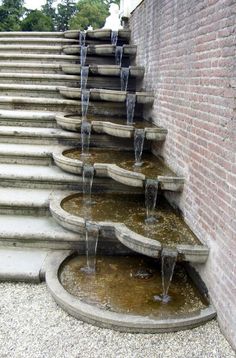 several water fountains are lined up against a brick wall in front of steps that lead down to the ground