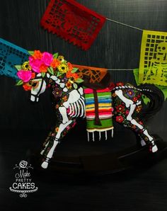 a wooden rocking horse decorated with flowers and mexican paper decorations hanging from it's sides