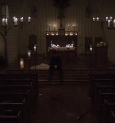 a man sitting in the middle of a church with candles on the walls and pews