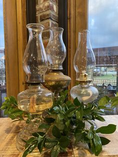 three glass vases sitting on top of a wooden table next to a green plant