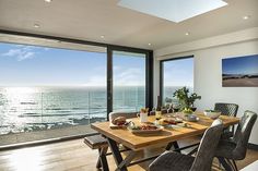 a dining room table with two chairs next to an open window looking out at the ocean