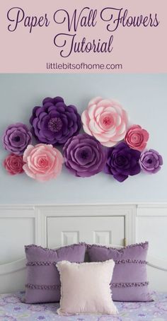 paper flower wall hanging on the side of a bed with purple and pink flowers above it