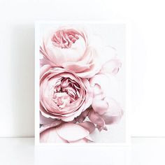 a card with pink flowers on it sitting next to a white wall and a plant