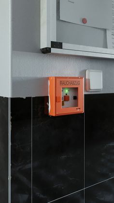 an orange box on the side of a white wall next to a black tile floor