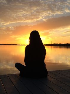 a woman sitting on a dock watching the sunset