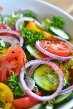 a salad with tomatoes, cucumbers, onions and parsley in a white bowl