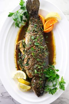 the fish is covered in sauce and garnished with parsley, lemon wedges and orange slices