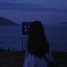 a woman is standing in front of the ocean at night with her back turned to the camera