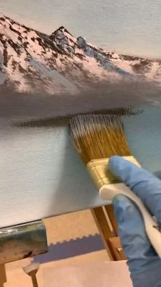 a person holding a paintbrush in their hand and painting a mountain scene on the wall