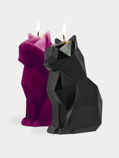 two black and pink candles sitting next to each other on a white surface with one candle in the shape of a cat