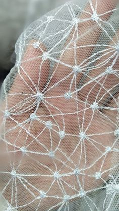 a close up of a person's hand wearing a white veil with small dots on it