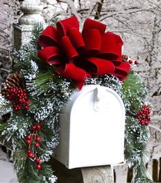 a white mailbox decorated with holly and red ribbon, surrounded by pine cones and berries