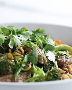 a white bowl filled with noodles, broccoli and meat