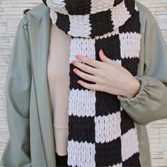 a woman wearing a black and white knitted scarf with her hands on her chest