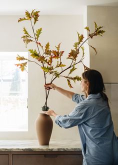 a woman is arranging leaves in a vase