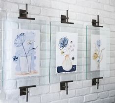 three glass frames are hanging on a brick wall with flowers in vases behind them