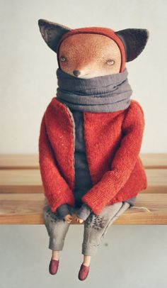 a stuffed animal wearing a red coat and scarf sitting on top of a wooden table