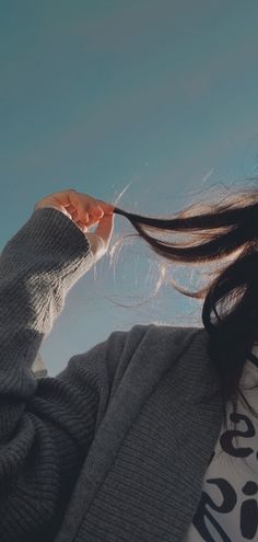 a woman with long hair is holding her hand up to her ear and looking at the sky