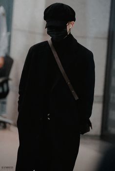 a person wearing a black coat and hat standing in front of a building with his back turned to the camera