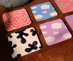 four square coasters with different designs on them sitting on a wooden table next to a rock