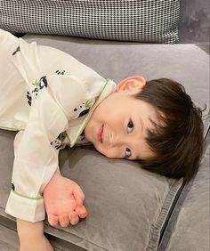 a young boy laying on top of a gray couch next to a black and white pillow