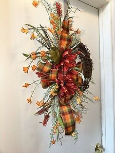 a wreath hanging on the front door with orange flowers and greenery in fall colors