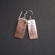 Majestic Tamarack pines are silhouetted against the glow of raw copper in these rustic and beautiful earrings. They are handcrafted from recycled copper and hang from sterling silver ear wires.  Measurements: Drop Length: 30mm (1 1/8in) Entire Earring Length: 45 mm (1 1/2in) Materials:  Copper  Copper is an element and a mineral known for its warm red-orange color, ductility, and malleability.  Copper has been used for thousands of years for jewelry and many people find that copper jewelry relie Rustic Copper Drop Earrings, Hammered Copper Earrings Rustica Jewelry, Nature-inspired Copper Earrings As Gift, Etched Copper Jewelry, Rust-colored Soldered Copper Earrings, Unique Patina Copper Earrings, Rivet Jewelry, Pmc Jewelry, Red Orange Color