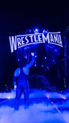 a man standing on top of a cloud filled stage holding up a sign that says wrestle mania