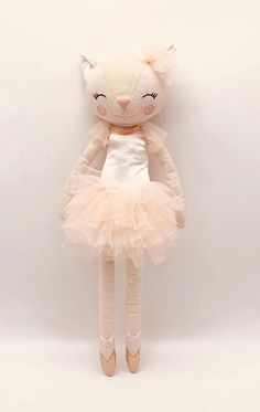 a stuffed cat in a pink tutu and ballet shoes is posed against a white wall