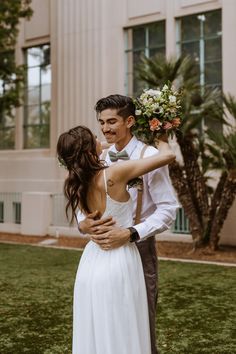 a bride and groom hugging in front of a building with palm trees on the lawn