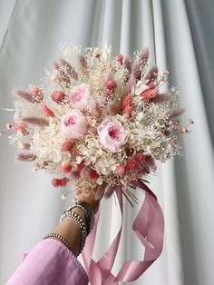 a woman's hand holding a pink and white bouquet with feathers on the side