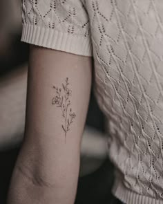 a woman's arm with a small flower tattoo on the back of her left arm