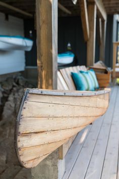 a wooden boat sitting on top of a wooden floor next to a porch with blue pillows