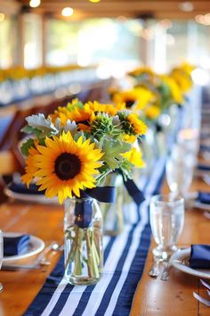 sunflowers are in vases on a long table with blue and white striped runneres