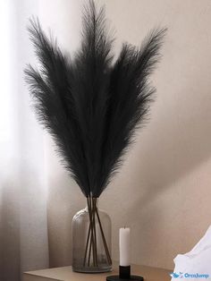 a vase with some black feathers in it on a table next to a white candle