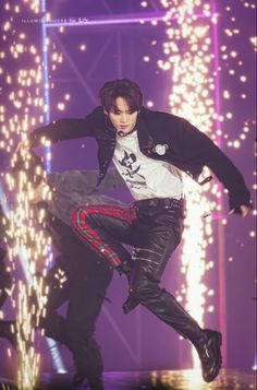 a male in a white shirt and black pants is dancing on stage with lights behind him