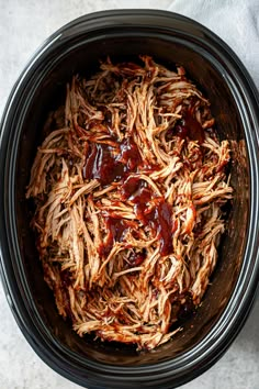 shredded pulled pork in a slow cooker with bbq sauce on the side, ready to be cooked