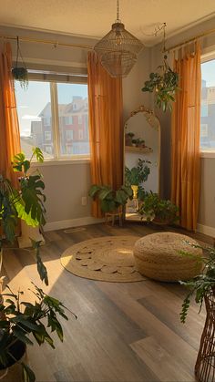 a living room filled with lots of plants next to a window covered in orange drapes